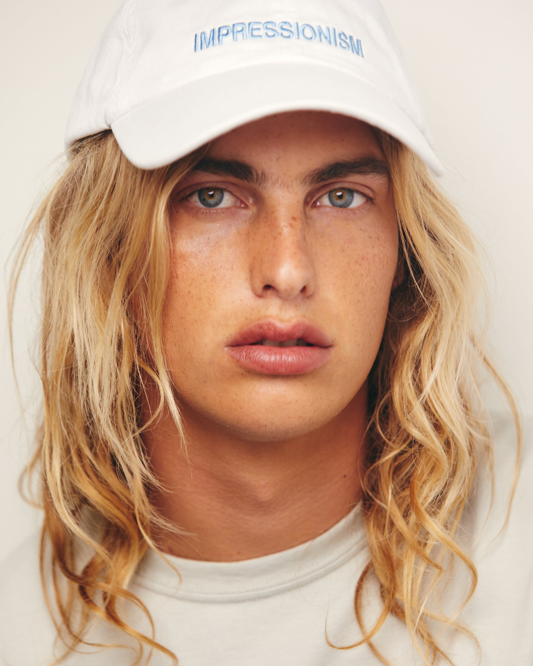 Lucas Ucedo wears White Baseball Cap / Dad Hat with Impressionism Art Movement Text Embroidery on Front. 100% Cotton.